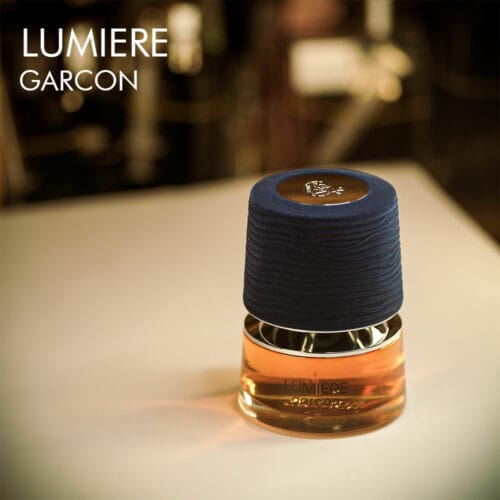 A 100ml bottle of French Avenue Lumiere Garcon Eau de Parfum with a orange-ish liquid and blue cap on a white table