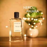 A 100ml bottle of Van Cleef & Arpels Neroli Amara Eau de Parfum with a transparent glass design and a black cap on a brown table.
