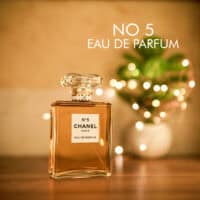 A 100ml bottle of Chanel No. 5 Eau de Parfum with a clear cap, orange liquid, white label on a brown table.