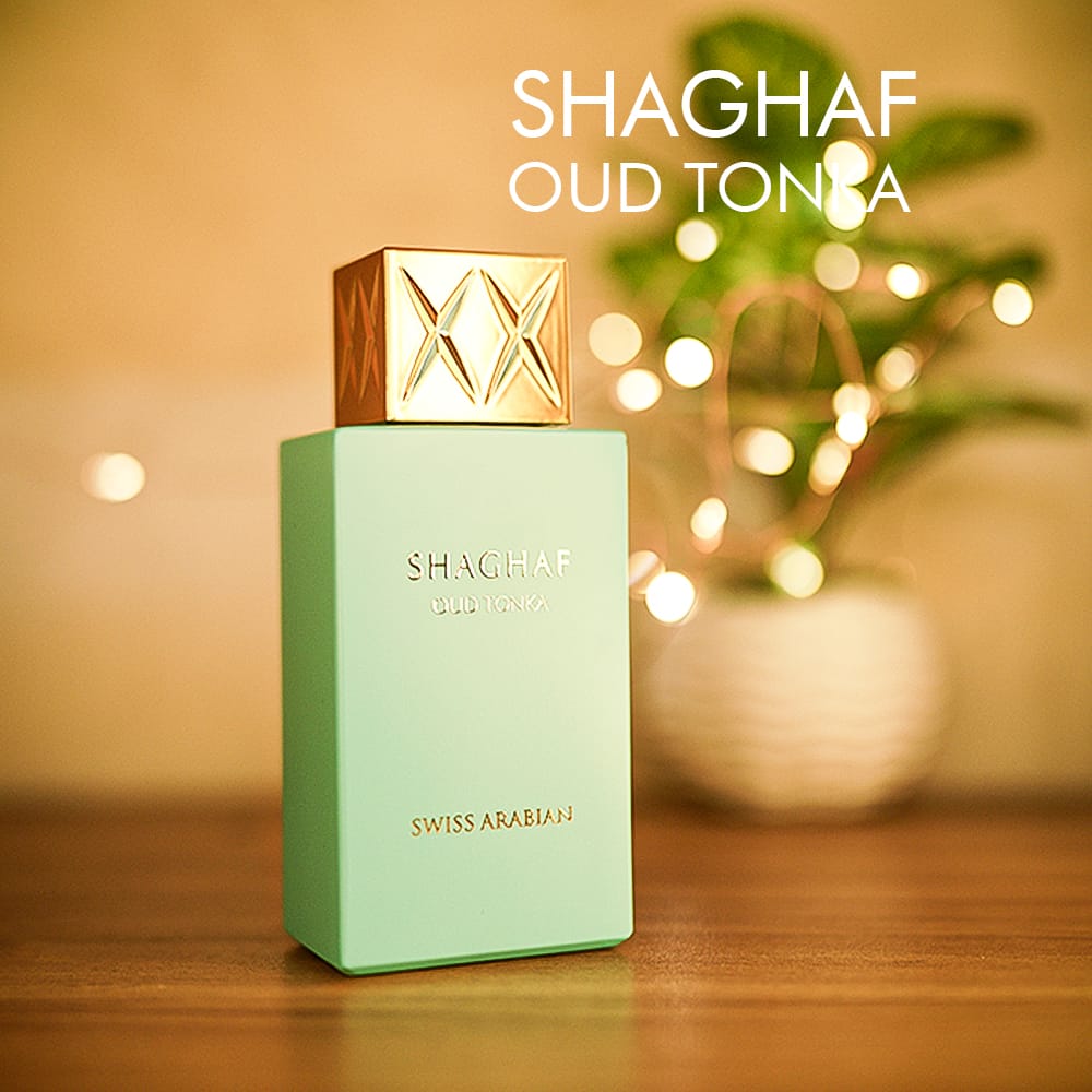 A 100ml bottle of Swiss Arabian Shaghaf Oud Tonka Eau de Parfum with a teal glass body, gold details, and a gold cap on a brown table.