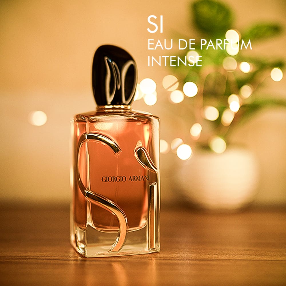 A 100ml bottle of Giorgio Armani Si Eau de Parfum Intense with a black cap and ornate gold design on clear glass bottle on a brown table.