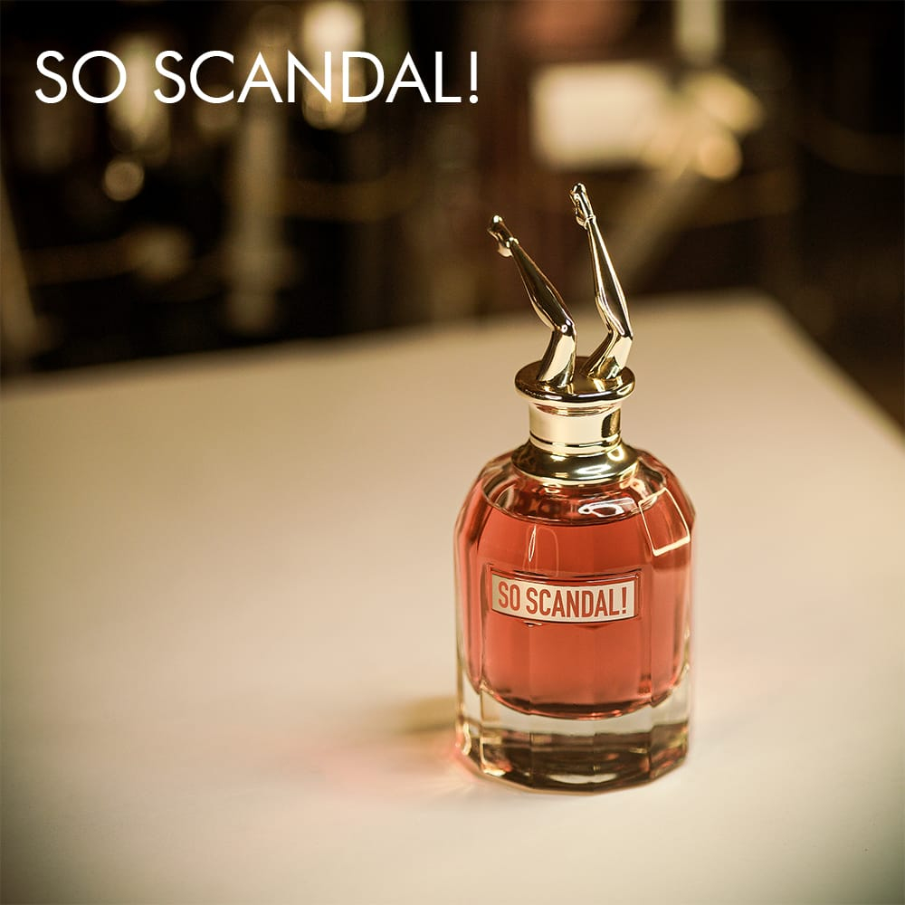 A 100ml bottle of Jean Paul Gaultier So Scandal! Eau de Parfum with reddish liquid, golden label and leg-shaped cap on a white table