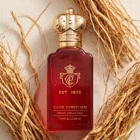39 Luxurious Clive Christian Crown Collection perfume in a deep red bottle with gold crown cap, resting on dried botanical twigs.