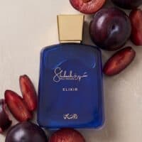 Singles (2) Vibrant blue men's cologne bottle surrounded by fresh plums and plum slices, showcasing luxurious fragrance and natural fruit essence.